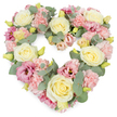 Set against a pure white background, this heart-shaped floral wreath appears soft yet defined, every curve carefully traced in blooms and foliage. The composition is dense and luxuriant, giving the impression of a floral pillow shaped into a perfect heart. Cream and pale yellow roses serve as key focal points, their sumptuous petals swirling outward to form full, rounded blooms that suggest warmth, devotion, and a gentle farewell. Between these, clusters of light pink carnations fill the spaces, their finely frilled petals layering over each other to create a tender, textured surface. Deeper pink and mauve lisianthus blossoms are dotted through the heart, their more open, trumpet-like forms and slight twists in the petals adding movement and a touch of quiet drama. Tiny yellow-green buds and hints of new growth can be seen peeking out among the larger flowers, subtly conveying renewal. Silvery eucalyptus leaves curve elegantly along the heart's outer edge and weave in among the blossoms, their rounded shapes and cool tones offering a soothing contrast to the warm creams and pinks. Altogether, the wreath feels calm, consoling, and deeply heartfelt, an ideal tribute to honour a loved one. It is easy to picture this arrangement resting beside a photograph at a Plaistow memorial service, or being carried through the streets towards a local chapel, its pastel colours softening the moment. The design reflects the sensitivity and care of a Plaistow florist who understands how flowers can speak when words feel insufficient, bringing a sense of peace and shared remembrance.